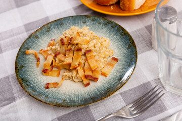 Dishes made from cereals and lard. Boiled oatmeal and fried pieces of bacon, simple rustic food, hearty dinner. Dish is decorated with sprig of parsley.