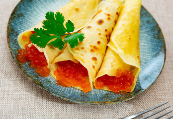 Service plate containing fried hotcakes with red caviar and necessary table laying