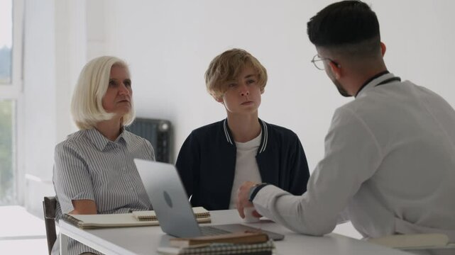 Grandmother and teenager son boy at doctor's for regular health check up examination. Male Indian pediatrician talk to parent of small kid guy visit. Medicine, pediatry for children