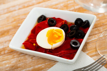 Mediterranean traditional roasted pepper salad served with eggs on wooden table.