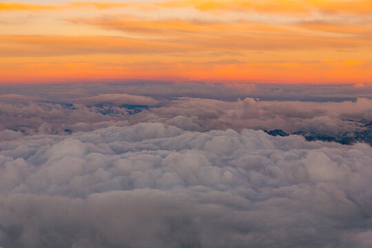 View through an aircraft window of sunset above clouds