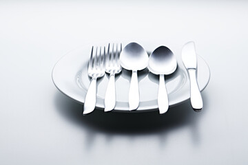 Silver colored cutlery such as spoons, forks, knives, cups and plates photographed against a white...