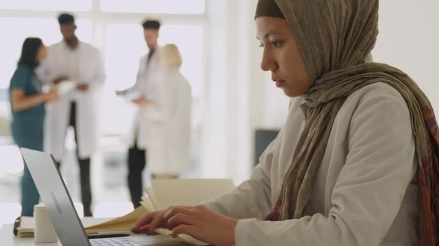 Happy smiling arabian nurse islamic doctor therapist wear white medical coat hijab sitting at clinic muslim female practitioner intern using laptop computer for medical healthcare service
