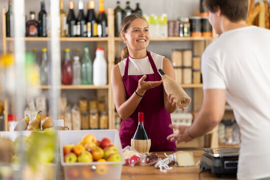 Young saleswoman in uniform sells bottle of wine to young male customer in grocery store