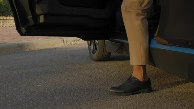 Low section of black businessman in trendy shoes leaving parked car and walking away during road trip in city.