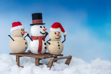 A joyful snowman and two sandy snowmen pose together for a Christmas and New Year celebration on a sled. Lot of snow, blue sky, this mix of winter and beach vibes brings a fresh holiday twist.
