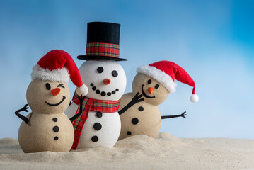 A joyful snowman and two sandy snowmen pose together for a Christmas and New Year celebration! With a snowy backdrop and blue sky, this mix of winter and beach vibes brings a fresh holiday twist.