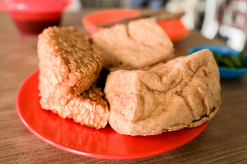 Fried tofu and fried tempeh in a red saucer