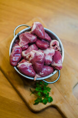 Raw duck hearts with parsley in metal pot on wooden chopping board . High quality photo