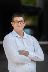 A successful businessman in a white shirt, with crossed arms, poses outdoors, confident expression on his face.