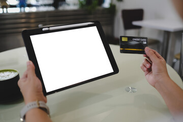 Modern digital payment scene showing hands holding a tablet with blank screen and credit card, set on a cafe table with matcha latte, capturing the essence of contemporary e-commerce.
