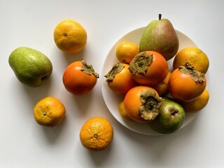 A colorful assortment of fresh fruits is displayed, featuring oranges, persimmons, and pears