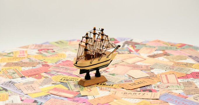 Ship model with sails on a bunch of vintage tickets from around the world, theater, movie, concerts, transport, boarding passes, hotel reception cards and other documents