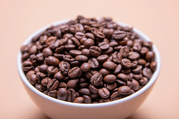 Roasted coffee beans in white ceramic bowl isolated on brown background
