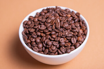 Roasted coffee beans in white ceramic bowl isolated on brown background