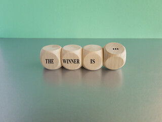Cubes form the expression The winner is... Beautiful blue background, grey table.
