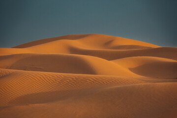 Views of the Dubai desert at sunset, footprints in the sand, with wind sweeping grains off the dunes.