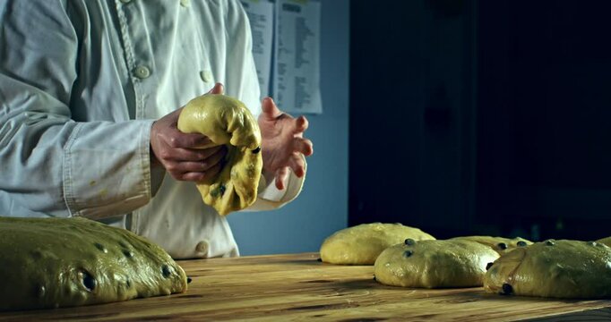 Super slow motion macro of artisan baker kneading raw dough with chocolate pieces for homemade Italian panettone on rustic wooden table in bakery kitchen at 1000 fps.