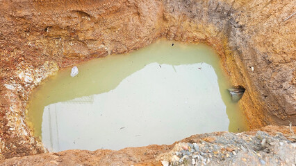 Excavation Site: A deep pit in the earth reveals a pool of murky water. Groundwater extraction