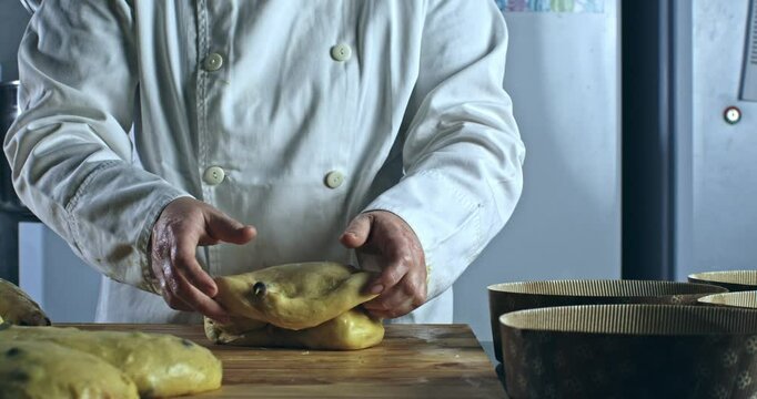 Super slow motion close up of artisan baker shaping of raw dough with chocolate pieces while kneading for homemade Italian panettone on rustic wooden table in bakery kitchen at 1000 fps.