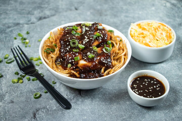 Teriyaki Fried Chicken Noodles with green onion, spicy sauce, cabbage salad and fork served in bowl isolated on grey background side view of asian food