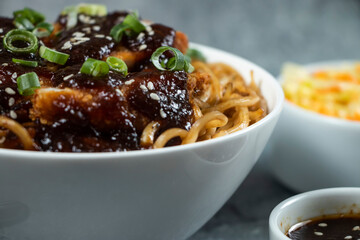 Spicy Teriyaki Fried Chicken Noodles with green onion, spicy sauce, cabbage salad and fork served in bowl isolated on grey background side view of japanese food