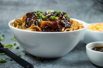 Teriyaki Fried Chicken Noodles with green onion, spicy sauce, cabbage salad and fork served in bowl isolated on grey background side view of japanese food