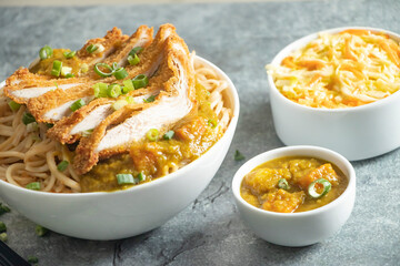 Katsu Chicken Noodles with potato curry, cabbage salad, green onion and fork served in bowl isolated on grey background closeup side view of japan food