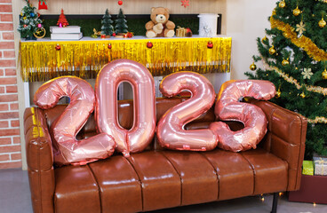 Number 2025 rose gold balloons on sofa New Year festival decorations for a party present gift boxes ornaments near Christmas tree in living room at home, Season's greetings celebration holiday concept