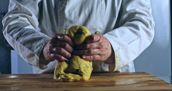 Super slow motion macro of artisan baker kneading raw dough with chocolate pieces for homemade Italian panettone on rustic wooden table in bakery kitchen at 1000 fps.