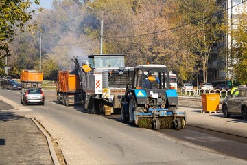 View of a milling machine and a tractor removing asphalt from a road during road works at a construction site.