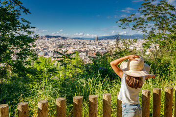 A back view of a little girl in a straw hat, overlooking Barcelona’s cityscape from a high point, capturing the city’s architectural allure