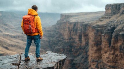 A hiker in a bright yellow jacket and orange backpack gazes out over a dramatic canyon landscape under overcast skies, embracing the beauty of nature