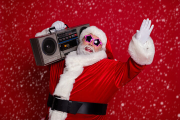 Photo of cool overweight santa listen boom box wear hat eyewear coat isolated on red background © deagreez