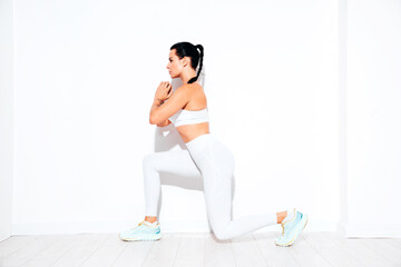 Fototapeta premium Fitness confident woman in white sports clothing. Sexy young beautiful model with perfect body. Female isolated on white wall in studio. Stretching out before training, makes lunges