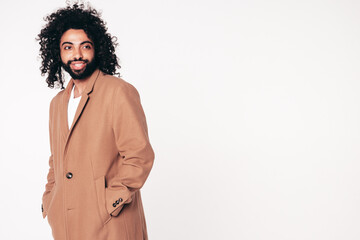 Handsome smiling hipster model.  Unshaven Arabian man dressed in brown coat clothes. Fashion male with long curly hairstyle isolated on white in studio. Cheerful and happy