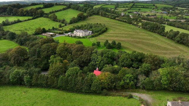 Saint Peter's Tin Church, Laragh, County Monaghan, Ireland, September 2022. Drone orbits counter clockwise in a wide view pushing closer to the distinctive red roof building surrounded by trees.