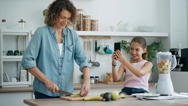 Video of  cute girl recording her mother with smartphone while making healthy fruit juice together in the kitchen 