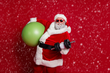 Photo of handsome strong santa claus wear red costume hat dark holding fitball building muscles isolated red color background