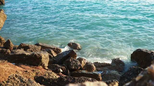 Waves gently lap at rocky shore during stunning sunset over ocean. Golden sunlight reflects off waves as they roll onto shore, creating tranquil atmosphere at sunset by sea. Montenegro summer, Canj.