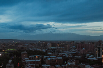 Views of Erevan under a dramatic sky with mountains in the background during twilight hours