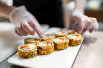 Close-up of gloved hands preparing sushi rolls on a white plate, showcasing the precision and freshness of Japanese cuisine. Ideal for culinary, food preparation, and restaurant themes.