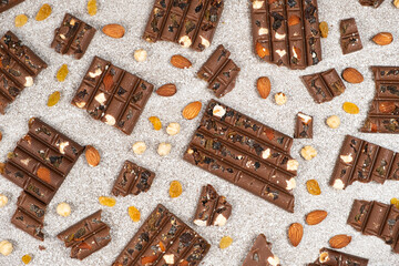 Broken chocolate pieces with nuts and raisins on a stone background top view