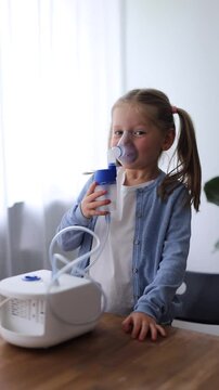 A 5-year-old girl at home uses a nebulizer, taking deep breaths to aid her respiratory health