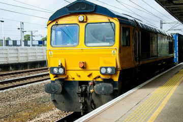A Large And Powerful Freight Train Passing By A Station Platform Pulling It's Carriages