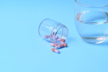 Medicines, pills and a glass of water next to it, on a blue background and inside a small glass container.