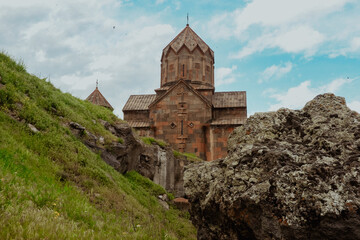 Historic Armenian monastery set against a lush green hillside on a cloudy day
