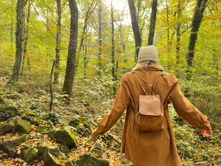 A woman wearing a brown coat and a white hat is walking through a forest