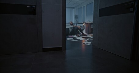 Dolly shot of depressed businessman sitting on floor after fit of rage over failed business deal or receiving bad news. Stressed office employee in destroyed office room. Financial crisis or firing.