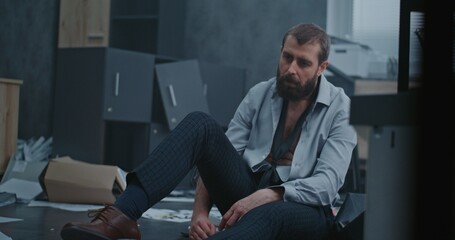Frustrated office worker sits on the floor, breathes heavily after destroying office room....